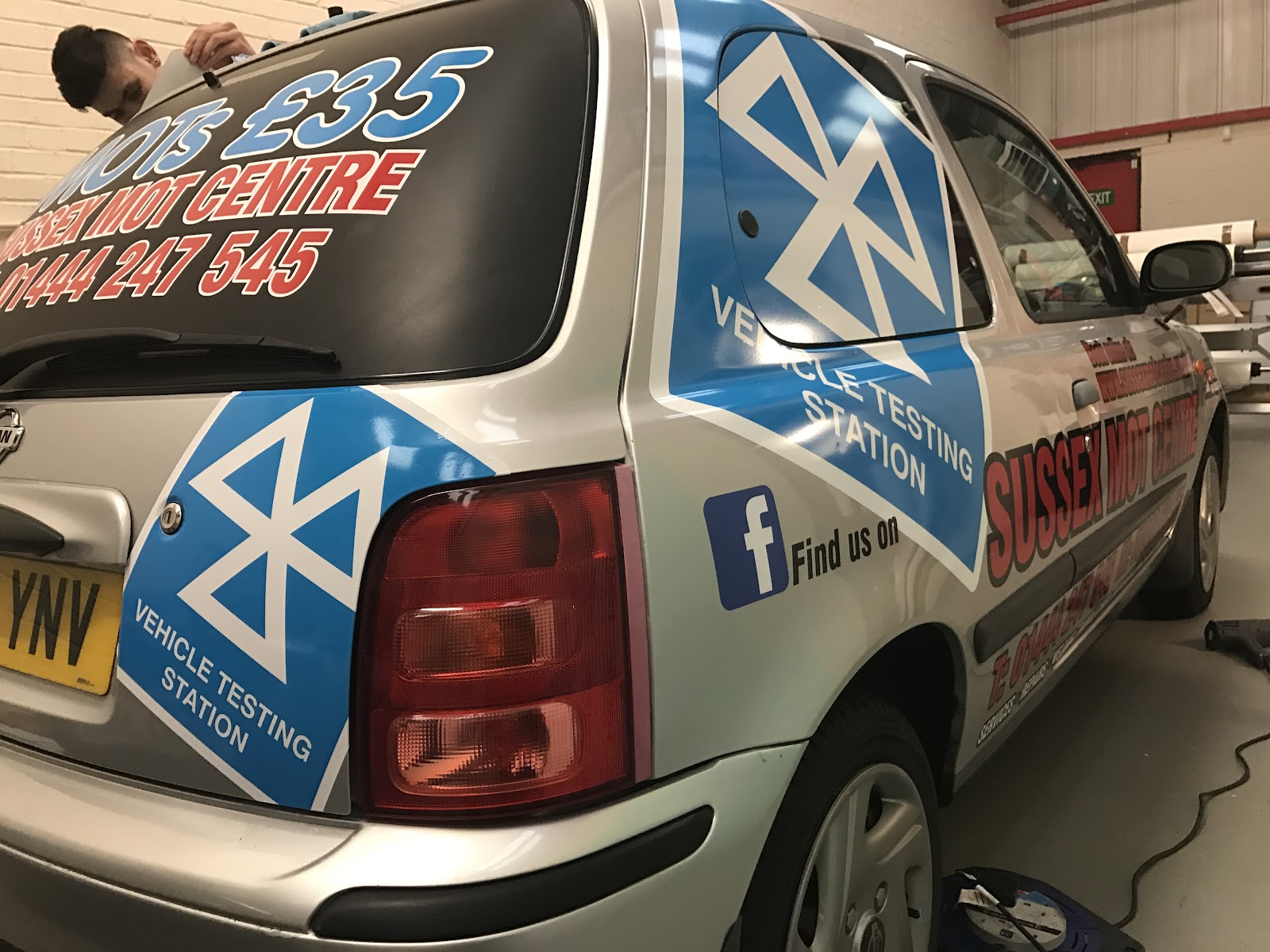 AMD Innovation applying a blue and silver graphic wrap to a Sussex MOT Centre car